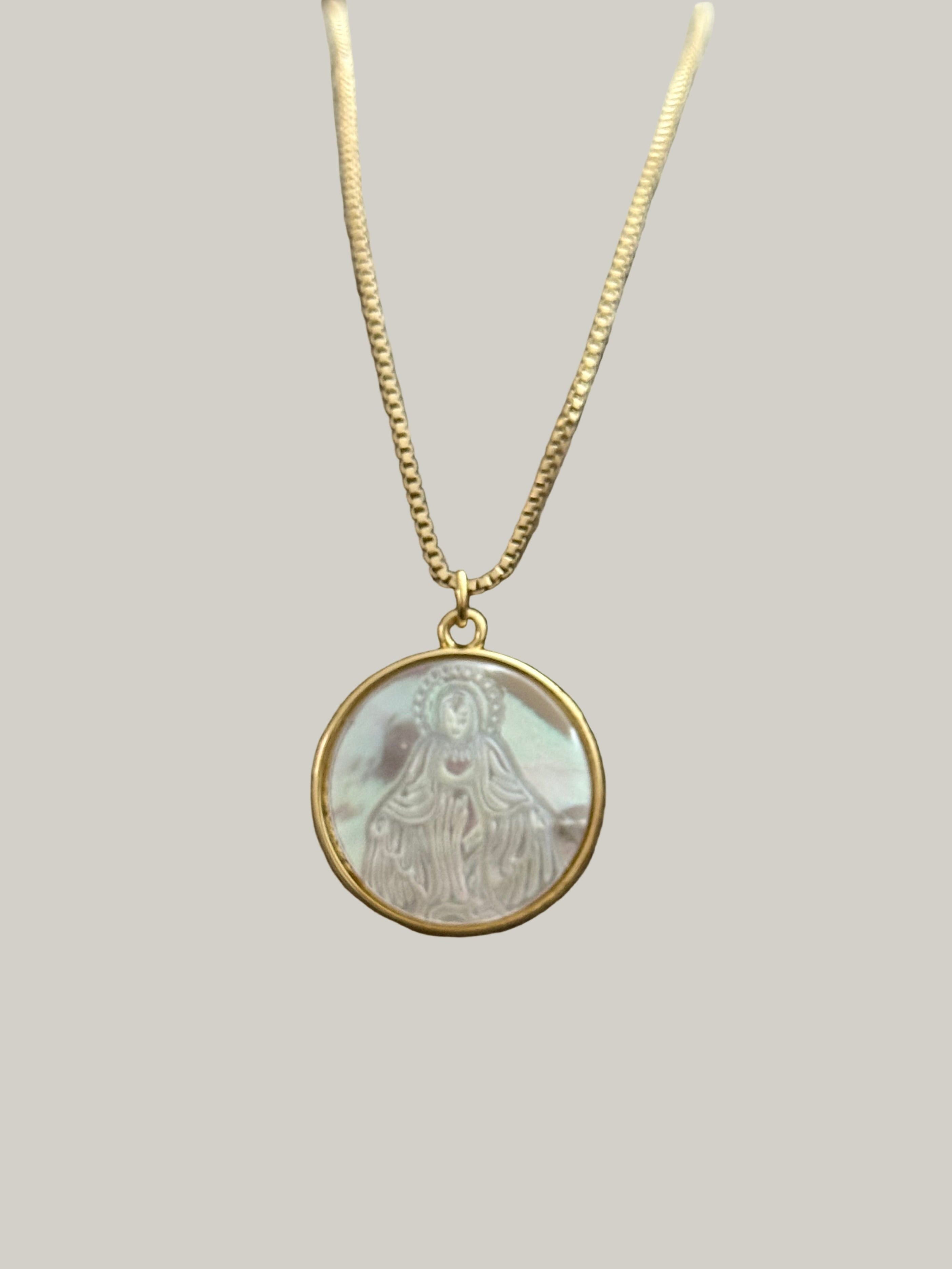 Gold necklace with a round pendant featuring a religious design on a light gray background